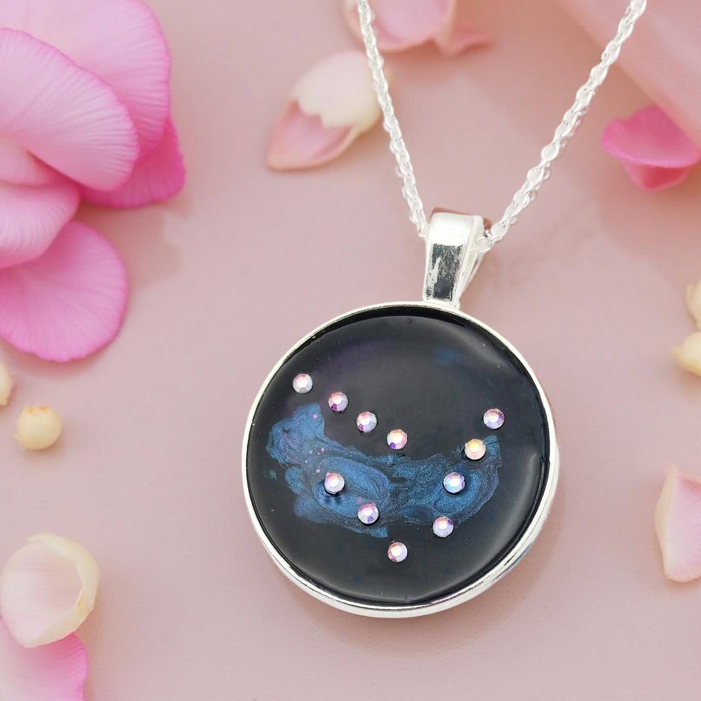 Dark blue with iridescent sparkling swirls of pinks, purples, silver, and monochromatic shades of blue enamel. With handset Aurora Borealis rhinestones to represent the star of the constellation of Capricorn. The pendant is 1 inch silver toned with a 1/4th inch bail on a silver toned chain.