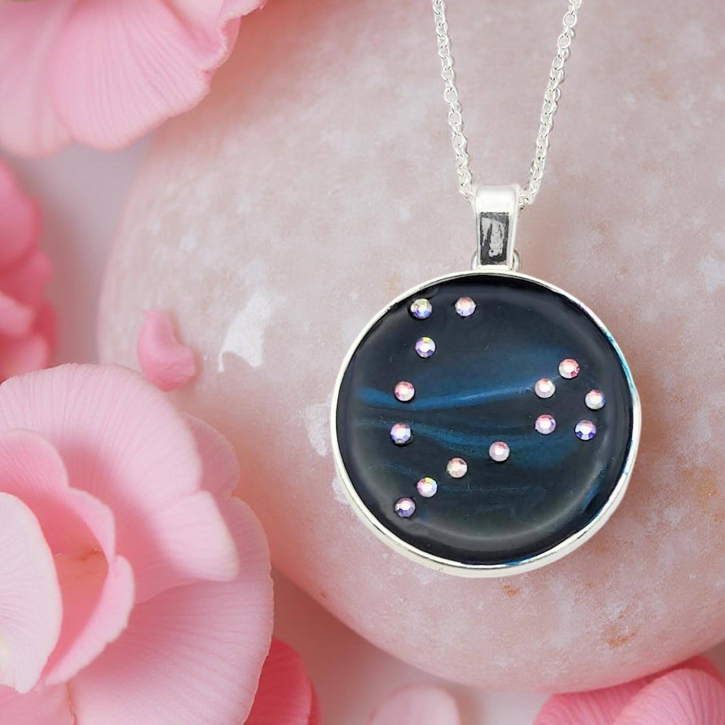 Dark blue with iridescent sparkling swirls of pinks, purples, silver, and monochromatic shades of blue enamel. With handset Aurora Borealis rhinestones to represent the star of the constellation of Pisces. The pendant is 1 inch silver toned with a 1/4th inch bail on a silver toned chain.