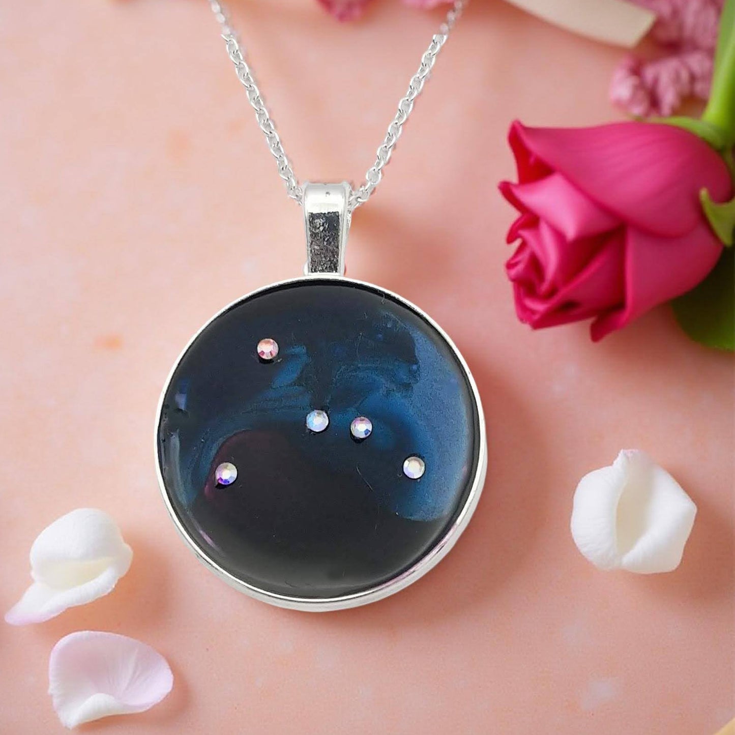 Dark blue with iridescent sparkling swirls of pinks, purples, silver, and monochromatic shades of blue enamel. With handset Aurora Borealis rhinestones to represent the star of the constellation of Cancer. The pendant is 1 inch silver toned with a 1/4th inch bail on a silver toned chain.