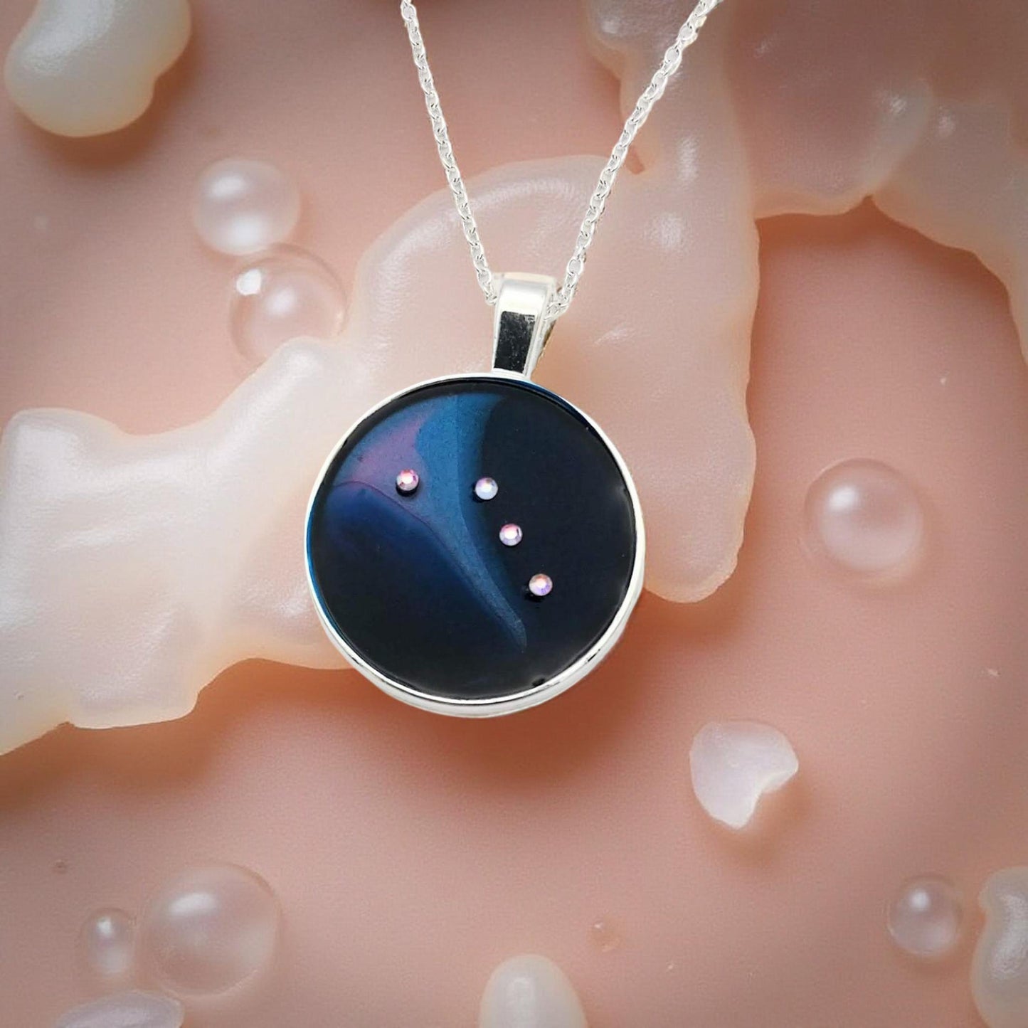 Dark blue with iridescent sparkling swirls of pinks, purples, silver, and monochromatic shades of blue enamel. With handset Aurora Borealis rhinestones to represent the star of the constellation of Aries. The pendant is 1 inch silver toned with a 1/4th inch bail on a silver toned chain.