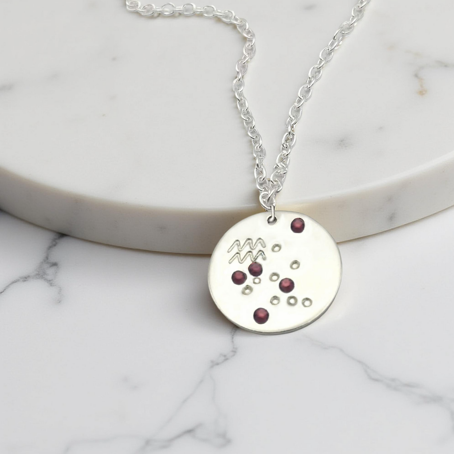 February Aquarius necklace pendant with hand set amethyst colored glass rhinestones forming the constellation of Aquarius. Hand stamped with the zodiac symbol for Aquarius, on a 3/4th of an inch silver toned circle hanging from a silver toned chain.