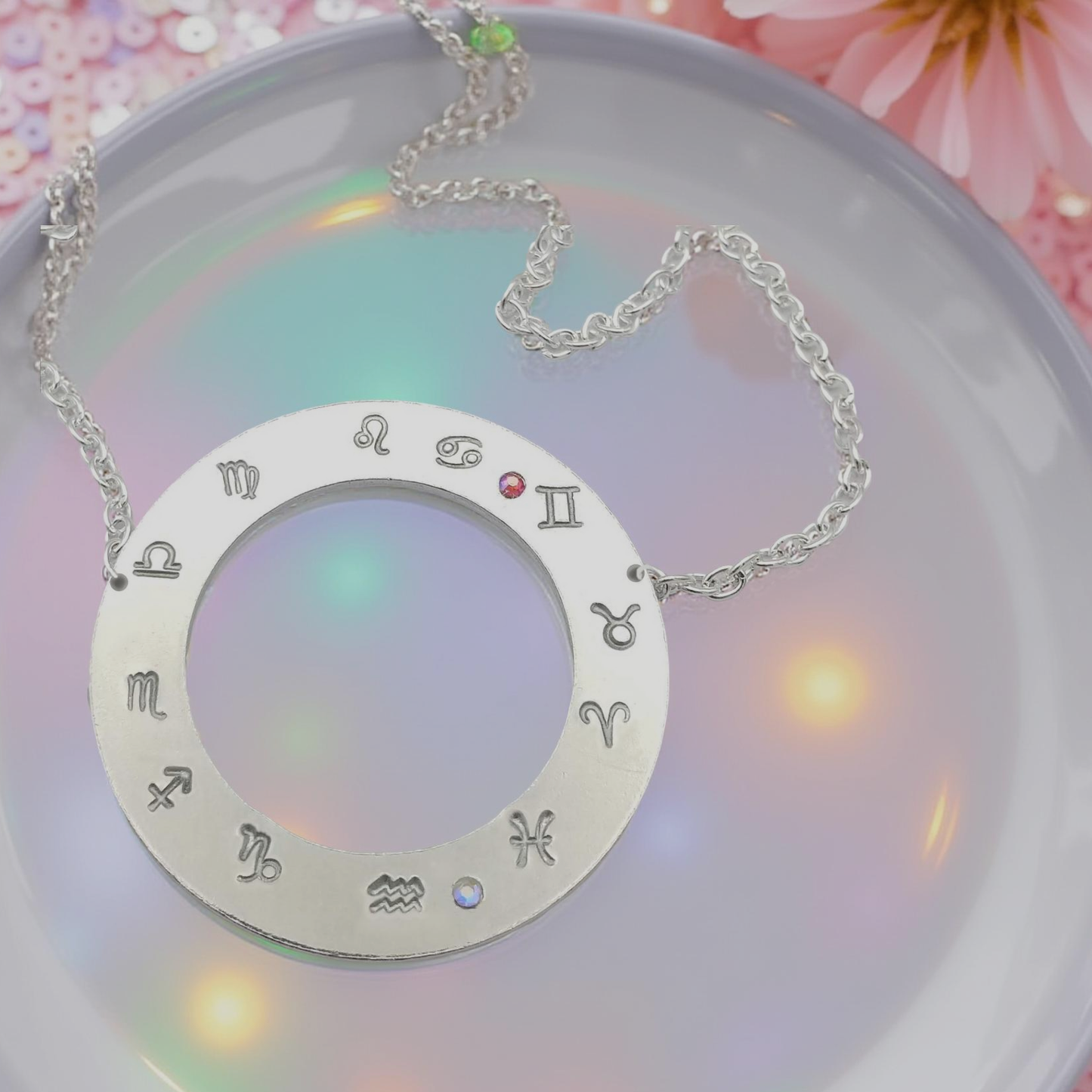 Hand stamped flat silver toned ring 1 ½ inch diameter pendant with all twelve zodiac symbols starting with your personalized rising sign on the 9 o'clock position. Followed by the rest of the astrology symbols in a counterclockwise motion, with handset iridescent red/orange and clear Aurora Borealis glass rhinestones, to represent your sun and moon signs. With a hollow inside diameter of 3/4th inch. Hanging from a 18 inch silver toned chain.