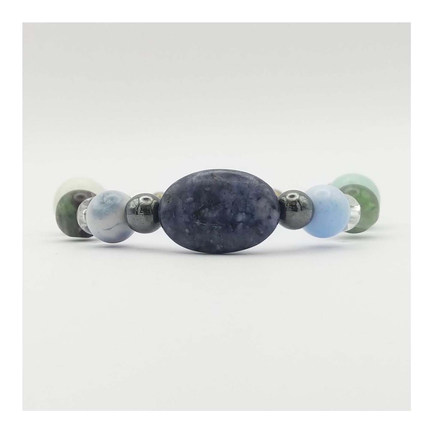 Mercury retrograde elastic bracelet with an oval blue sodalite bead at the center with other crystals such as blue lace agate, clear quartz, green and purple fluorite and other gemstones in a symmetrical pattern. In soothing cool tones along with hematite and pyrite which have a metallic finish.