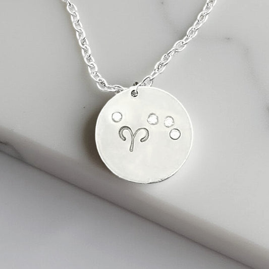 April Aries necklace pendant with hand set diamond colored glass rhinestones forming the constellation of Aries. Hand stamped with the zodiac symbol for aries, on a 3/4th of an inch silver toned circle hanging from a silver toned chain. 