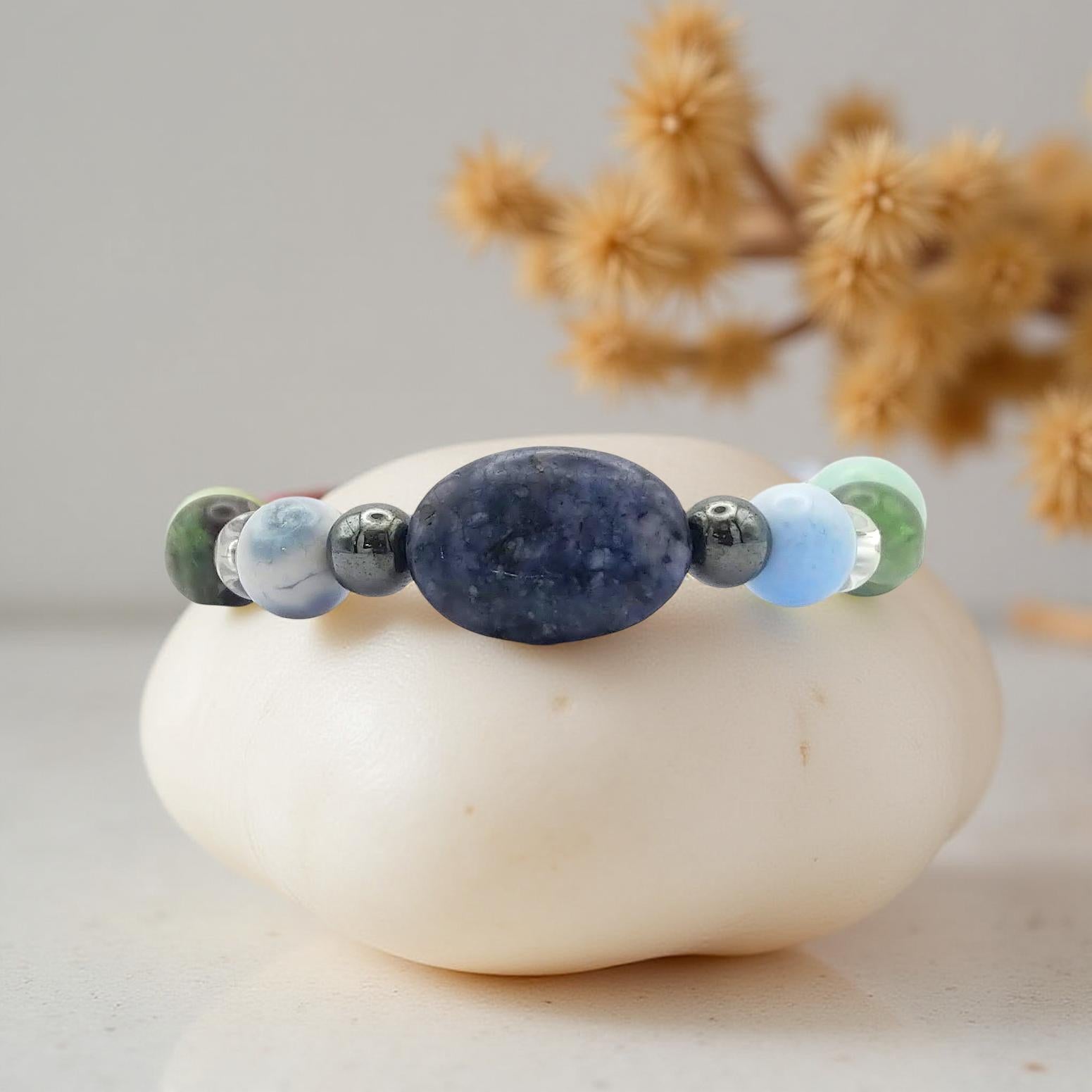 Mercury retrograde elastic bracelet with an oval blue sodalite bead at the center with other crystals such as blue lace agate, clear quartz, green and purple fluorite and other gemstones in a symmetrical pattern. In soothing cool tones  along with hematite and pyrite which have a metallic finish.