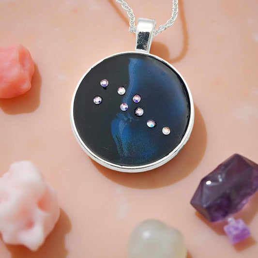 Dark blue with iridescent sparkling swirls of pinks, purples, silver, and monochromatic shades of blue enamel. With handset Aurora Borealis rhinestones to represent the star of the constellation of Taurus. The pendant is 1 inch silver toned with a 1/4th inch bail on a silver toned chain.