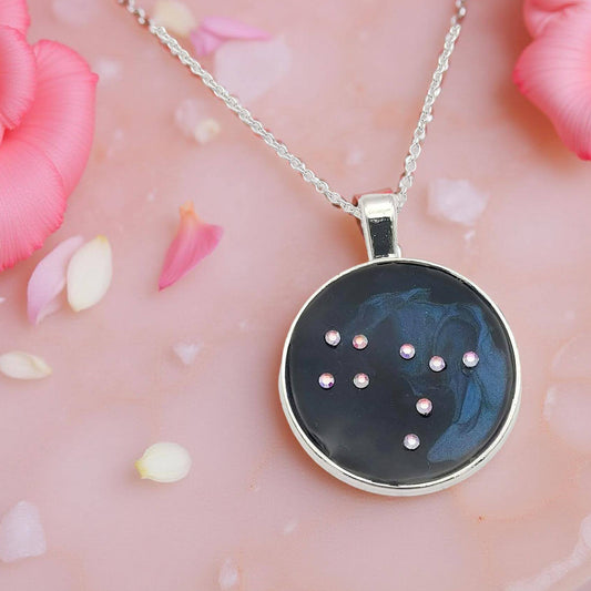 Dark blue with iridescent sparkling swirls of pinks, purples, silver, and monochromatic shades of blue enamel. With handset Aurora Borealis rhinestones to represent the star of the constellation of Gemini. The pendant is 1 inch silver toned with a 1/4th inch bail on a silver toned chain.