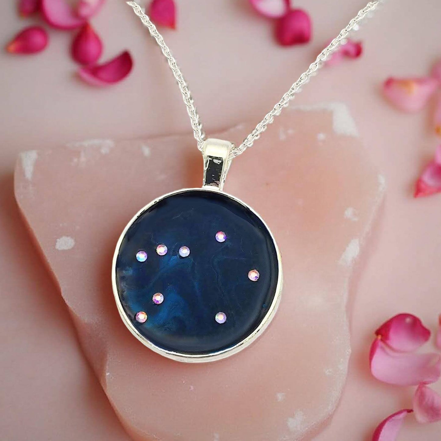 Dark blue with iridescent sparkling swirls of pinks, purples, silver, and monochromatic shades of blue enamel. With handset Aurora Borealis rhinestones to represent the star of the constellation of Libra. The pendant is 1 inch silver toned with a 1/4th inch bail on a silver toned chain.