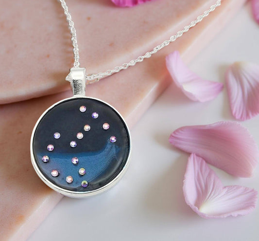 Dark blue with iridescent sparkling swirls of pinks, purples, silver, and monochromatic shades of blue enamel. With handset Aurora Borealis rhinestones to represent the star of the constellation of Scorpio. The pendant is 1 inch silver toned with a 1/4th inch bail on a silver toned chain.