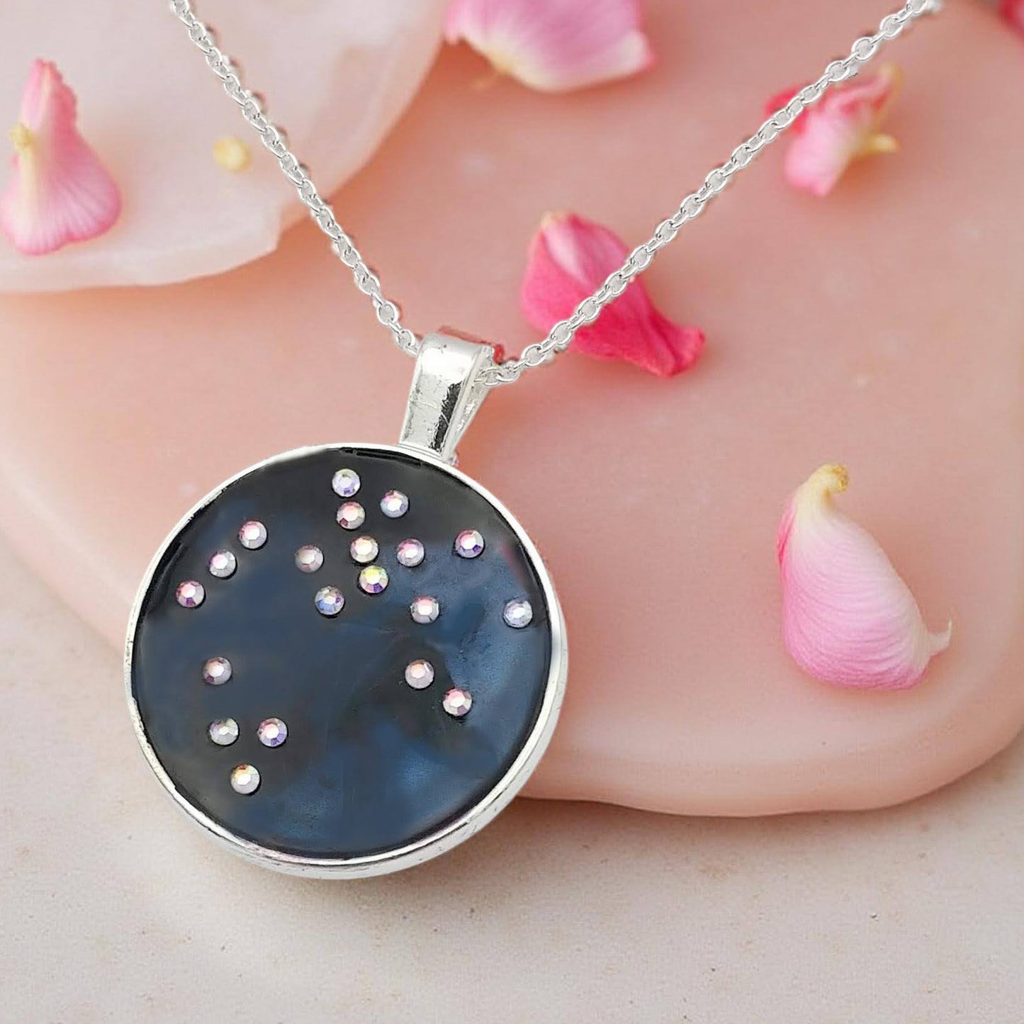 Dark blue with iridescent sparkling swirls of pinks, purples, silver, and monochromatic shades of blue enamel. With handset Aurora Borealis rhinestones to represent the star of the constellation of Sagittarius. The pendant is 1 inch silver toned with a 1/4th inch bail on a silver toned chain.