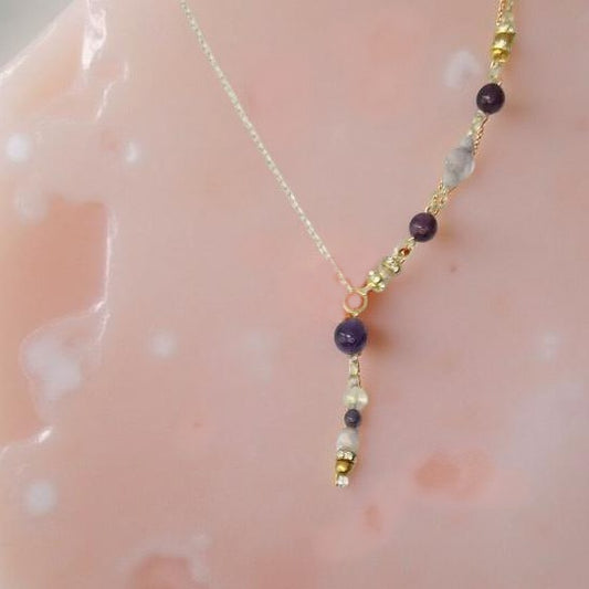Amethyst round beads with lavender and gold colored accents down one side of the gold toned necklace and a 2 ¼ inch drop. The other side of the necklace is a plain gold toned chain, equaling 18 inches around.  