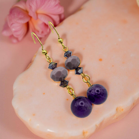 Amethyst, monochromatic purple and iridescent beads a-lined on a 2 inch drop earring on gold toned fish hooks. 