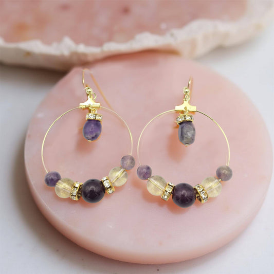 Round Amethyst, lavender and gold colored accented beads in a symmetrical pattern on 1 1/2 inch diameter thin gold hoop. With a small oblong amethyst bead, hanging for the top of the hoop, on gold toned fish hooks totally a 2 ½ inch drop. 