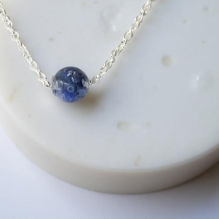 A ½ inch diameter single bead made of chipped sodalite encased in resin. Hanging from a 20 inch long silver toned chain.