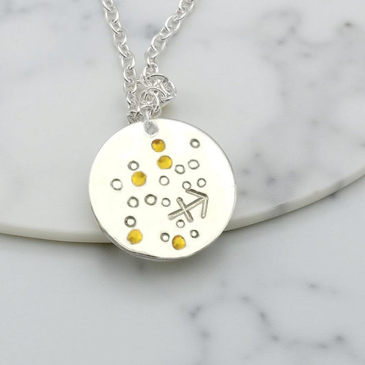 November Sagittarius necklace pendant with hand set citrine colored glass rhinestones forming the constellation of Sagittarius. Hand stamped with the zodiac symbol for Sagittarius, on a 3/4th of an inch silver toned circle hanging from a silver toned chain.