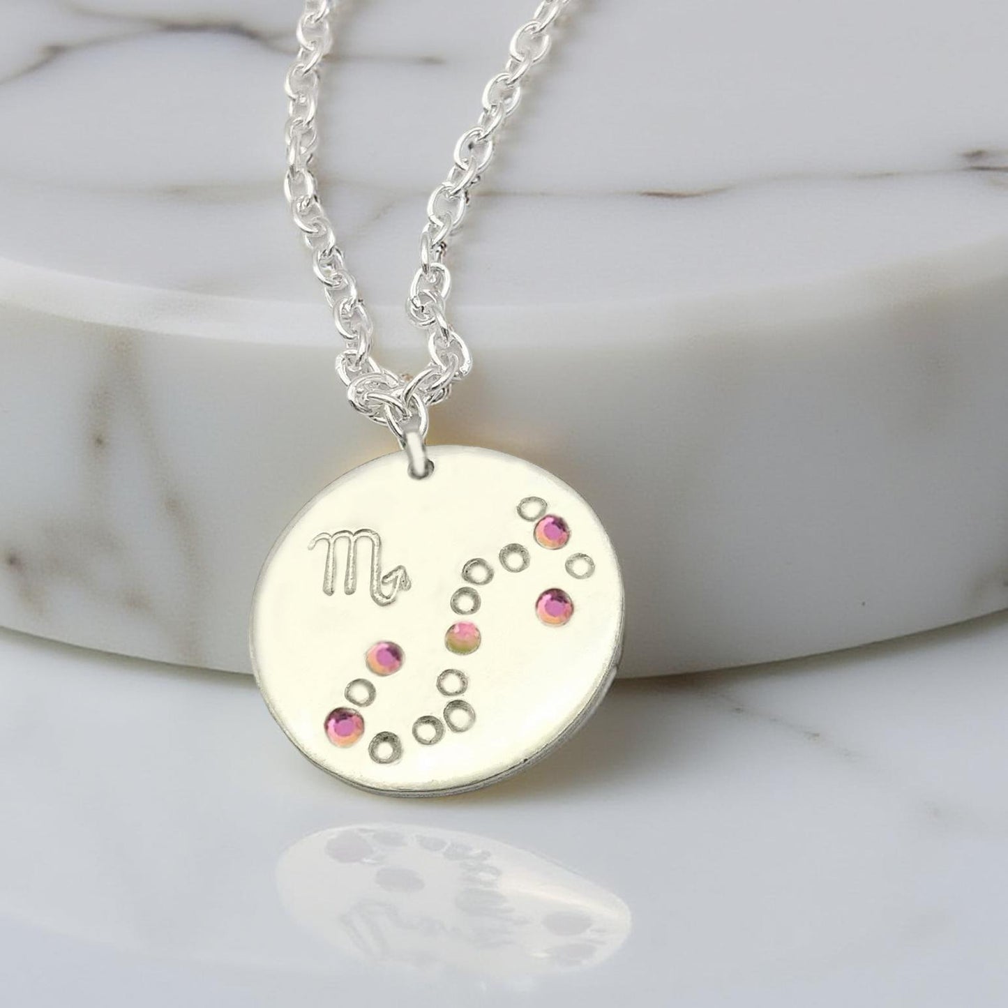 October Scorpio necklace pendant with hand set tourmaline colored glass rhinestones forming the constellation of Scorpio. Hand stamped with the zodiac symbol for Scorpio, on a 3/4th of an inch silver toned circle hanging from a silver toned chain