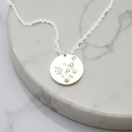 August Virgo necklace pendant with hand set peridot colored glass rhinestones forming the constellation of Virgo. Hand stamped with the zodiac symbol for Virgo, on a 3/4th of an inch silver toned circle hanging from a silver toned chain.
