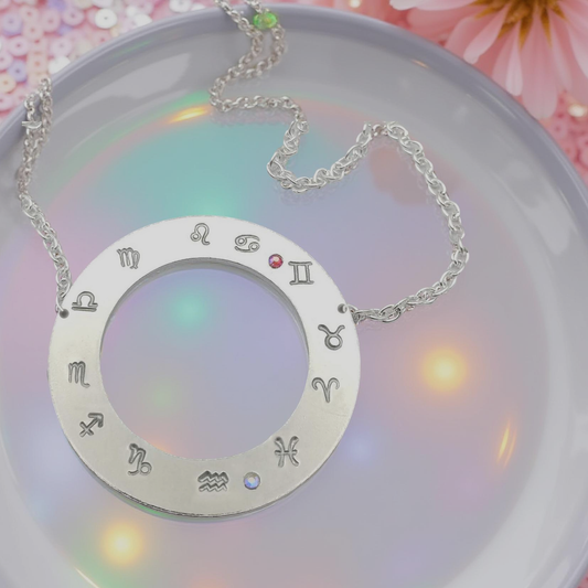 Hand stamped flat silver toned ring 1 ½ inch diameter pendant with all twelve zodiac symbols starting with your personalized rising sign on the 9 o'clock position.  Followed by the rest of the astrology symbols in a counterclockwise motion, with handset iridescent red/orange and clear Aurora Borealis glass rhinestones, to represent your sun and moon signs. With a hollow inside diameter of 3/4th inch.  Hanging from a 18 inch silver toned chain.     